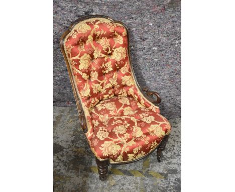A late Victorian walnut framed nursing chair with a floral carved crest and scrolled arms, button upholstered in a cream and 