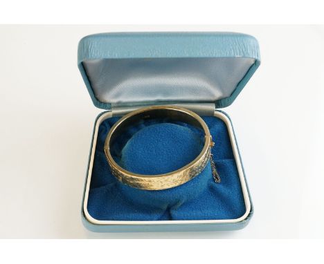 9ct yellow gold hinged bangle, engraved floral and foliate decoration to the upper half, tongue and box clasp with safety cha