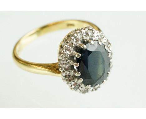 Sapphire and diamond 18ct yellow and white gold set cluster ring, the oval mixed cut dark blue sapphire measuring approx 9.5m