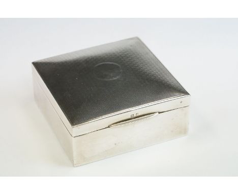 Silver cigarette box of square form, engine turned hexagonal repeating decoration to the hinged lid, vacant circular cartouch