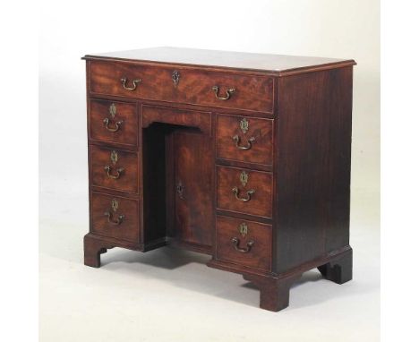 A George III mahogany kneehole desk, containing an arrangement of seven short drawers, about a central recessed cupboard, on 