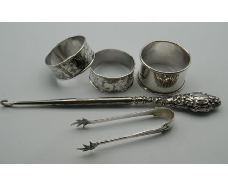 Three silver napkin rings, a pair of silver tongs and a button hook. 67.7 grammes of weighable silver.