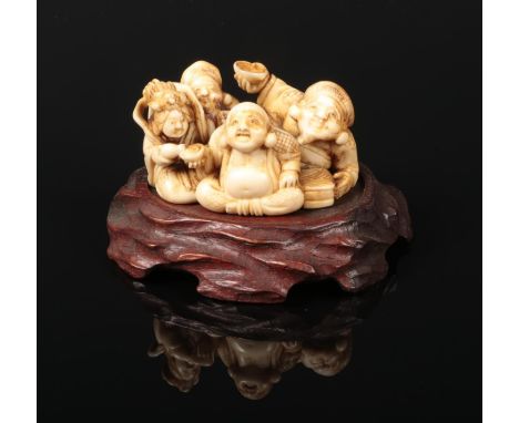 A Japanese Meiji period carved ivory large netsuke on carved hardwood plinth. Formed as a group of four seated figures. Signe