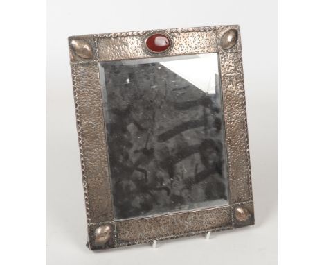 An Arts &amp; Crafts planished silver mounted mirror in the manner of Archibald Knox. Set with a claret enamel roundel to the