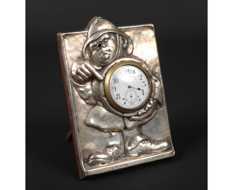 An Edwardian silver mounted oak strut clock. Embossed with a caricature of a policeman holding and pointing to the clock face
