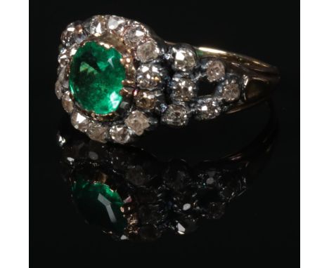 A Georgian gold and silver mounted emerald and diamond cluster ring. With a cushion cut emerald 6mm square under a border of 