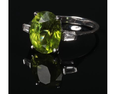 An Art Deco style 18 carat white gold peridot and diamond ring. Set with a large faceted ovoid peridot 11mm x 9mm, flanked by