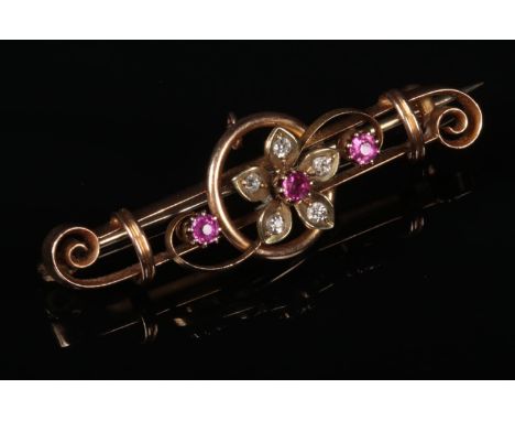 A 15 carat gold ruby and diamond bar brooch. Of open scrollwork form and with floriform centre, 42mm wide.  Good condition.