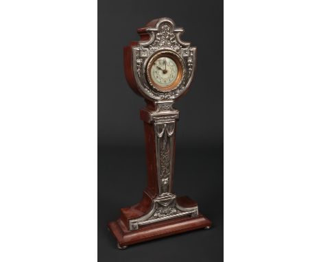 An Edwardian silver mounted mahogany pedestal mantel clock by W J Myatt &amp; Co. Decorated in relief with flowers and ribbon