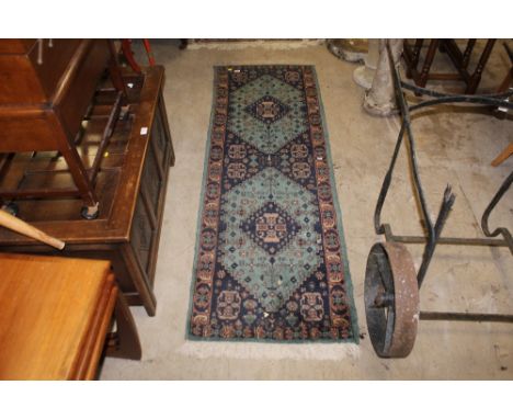 A Pakistani runner, woven in blues and muted colours with two stepped lozenge medallions on a green ground, 183 cm long x 63 
