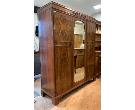 A figured walnut triple wardrobe, the frieze with scrolled acanthus decoration over an arched bevelled mirrored door to centr