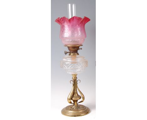 An Art Nouveau brass oil lamp, having floral etched pink glass handkerchief shade over cut crystal glass font, to scroll styl