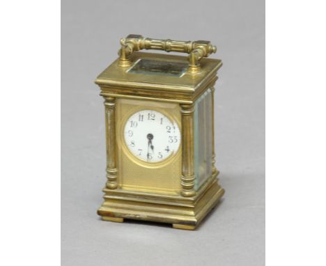 CASED MINIATURE BRASS CARRIAGE TIME PIECE, the enamelled dial inside an engine turned frame, the case with column corners, wi