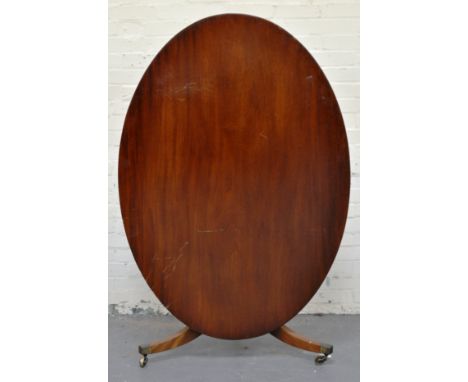 19th Century mahogany breakfast table, oval tilt top, ringed column, tripod fluted legs, brass castors. 100 x 143cms.