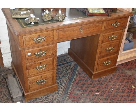 Light oak kneehole pedestal desk of nine drawers with tooled green leather top and having brass handles