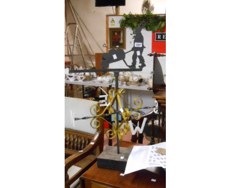 A vintage wrought iron weather vane with scroll decoration and gardener vane set on wood block mount