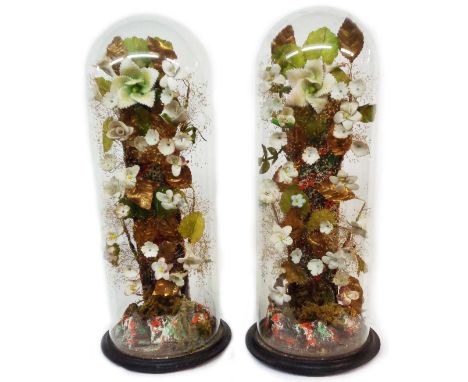 A pair of old glass dome mantel decorations containing ceramic flowers and foliage set on wooden plinths