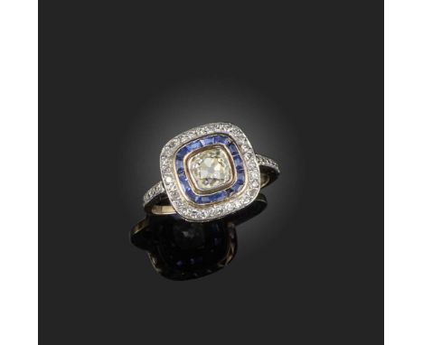 A sapphire and diamond cluster ring, set with a cushion-shaped diamond within radiating border of calibré-cut sapphires and s