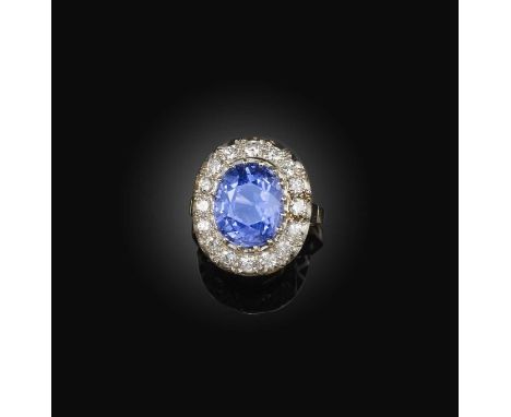 A sapphire and diamond ring, of cluster design, claw-set with an oval sapphire weighing 9.28 carats, within a border of brill