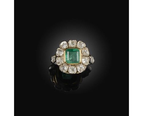 An emerald and diamond ring, early 20th century, designed as a floral cluster, collet-set with a step-cut emerald weighing ap