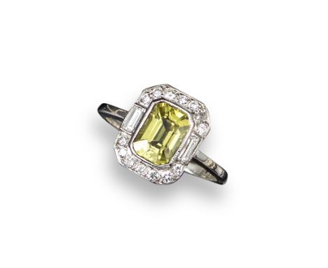 A yellow sapphire and diamond cluster ring, the emerald-cut sapphire is set within a surround of round brilliant and baguette