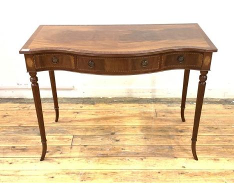 A Regency style inlaid mahogany console table of serpentine outline, the cross banded top with reeded edge over three drawers