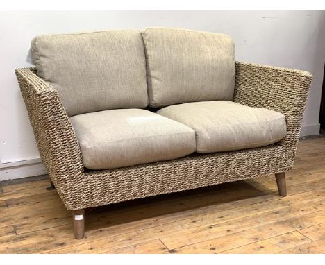 A wicker veranda two seat sofa, with oatmeal upholstered squab cushions, raised on turned supports, H92cm, W149cm. D86cm