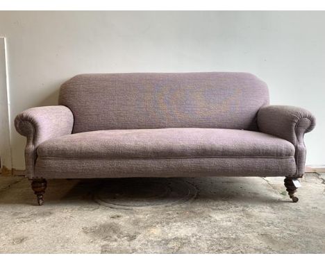 A Victorian three seat sofa, upholstered in a mottled lilac fabric, raised on turned walnut front supports with brass and cer