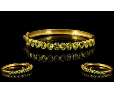 Peridot Oval Hinged Bangle, a row of oval cut peridots totalling 6cts, bezel set, vertically, along the front of the hinged b