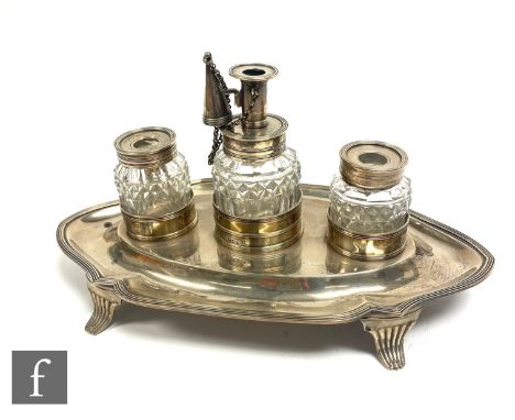 A George III silver desk stand, the oval stand raised on swept reeded supports with two inkwells and central oil lamp, London