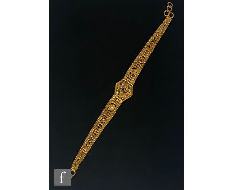 An Indian 22ct gold bracelet with central pierced hexagonal panel flanked by tapering ornate chain detailed with red and gree