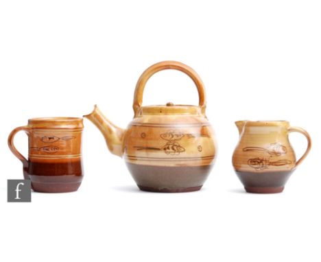 Three pieces of Winchcombe Pottery comprising a tea kettle, a mug and a milk jug each decorated with hand painted fish in ton