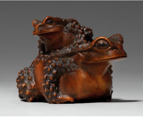 Okimono-Netsuke. Auf dem Rücken einer massigen Kröte sitzt ein zweites, kleineres Tier. Die Augen jeweils eingelegt aus schwa