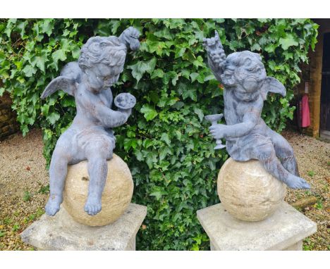 A PAIR OF CAST LEAD CHERUBS UPON COMPOSITION STONE SPHERESone holding grapes aloft with goblet in the other hand, the other h