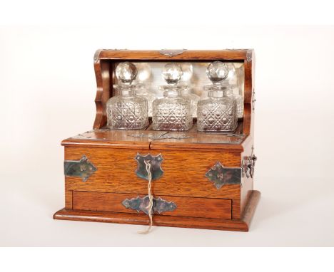 AN EDWARDIAN OAK TANTALUS GAME COMPENDIUMearly 20th century, white metal strapwork and carrying handles, contains three cut g