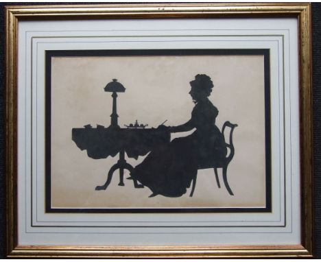 A large silhouette picture of a Victorian lady writing at a tripod table supporting a lamp, inkstand and books, 24.5 x 34cm 