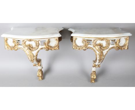 A pair of modern Rococo style white painted and gilt carved wooden console tables with shaped marble tops, height 60cm, width