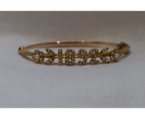 A Victorian yellow metal hinged bangle having a seed pearl applique date panel of 1892, no marks, tested as 15ct gold, with o