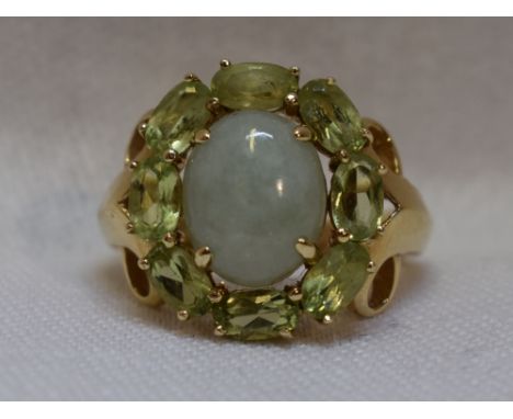 A lady's dress ring having an oval jade cabouchon within a peridot set border to shaped shoulders on a yellow metal loop stam