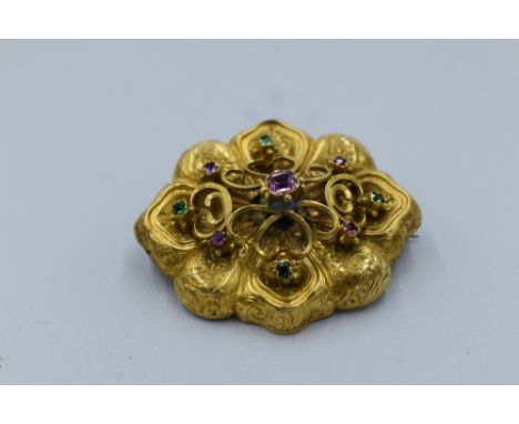 A yellow metal locket brooch having pink and green collared stones to a raised setting to engraved shaped panel with hair loc