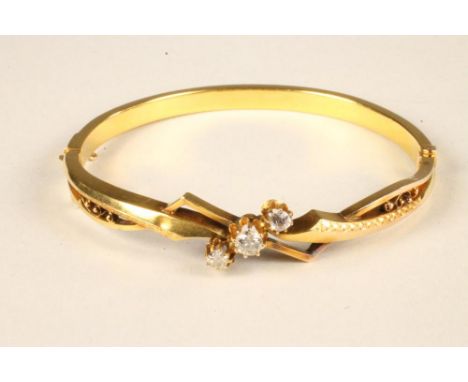 A LATE VICTORIAN GOLD STIFF HINGED BANGLE, the upper section centred by three brilliant cut stones in a cross-over setting to