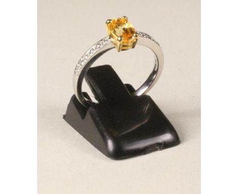 A YELLOW SAPPHIRE DRESS RING, the cushion cut stone claw set to shoulders pave set with six round brilliant cut diamonds and 