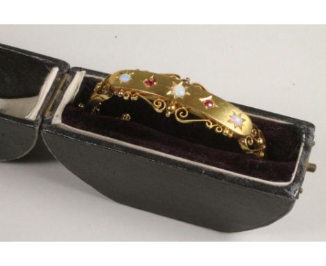 AN EDWARDIAN 9CT GOLD STIFF HINGED BANGLE, the upper section gypsy set with three cabochon polished opals and two facet cut r