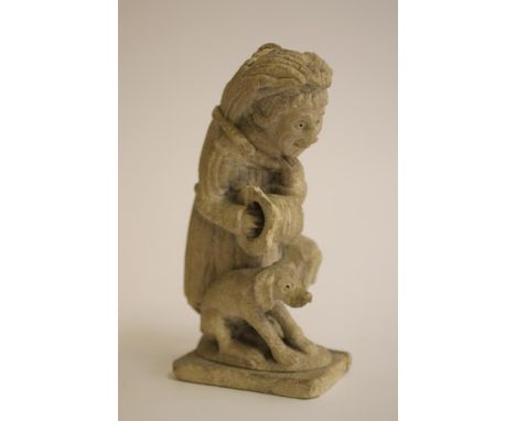 A LIMESTONE CARVING of a medieval monk, holding a hat in his right hand and basket over his left arm, carrying a sheaf of cor