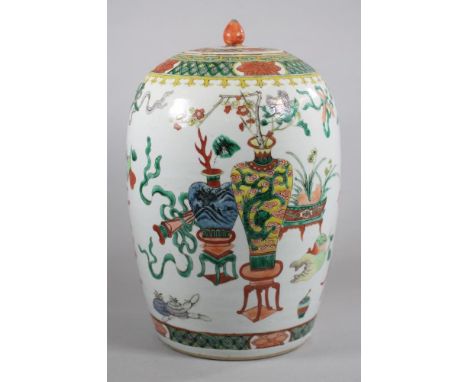 A CHINESE PORCELAIN JAR AND COVER of rounded cylindrical form, painted in polychrome enamels with precious objects on a table