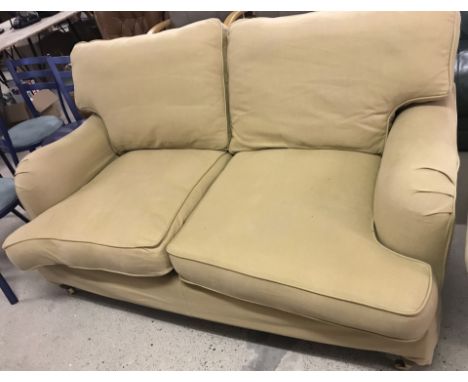 A vintage large two seater sofa with tan coloured removable covers. Castor feet to front fixed feet to back. Approx. 162 cm w