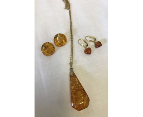 A large amber drop pendant on a goldtone chain. Together with a pair of button style amber stud earrings and a pair of goldto