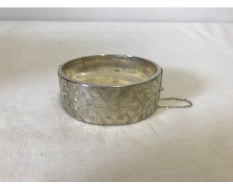A hallmarked silver bangle with safety chain. Birmingham 1964. 1 inch (2.5cm wide). Approx. 38.2g 