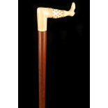 AN ANTIQUE WALKING CANE, the ivory coloured natural handle modelled as a booted foot, inlaid with