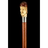 AN AMUSING GROTESQUE HEAD CANE, the stag horn (probably) carved face, set with glass eyes and